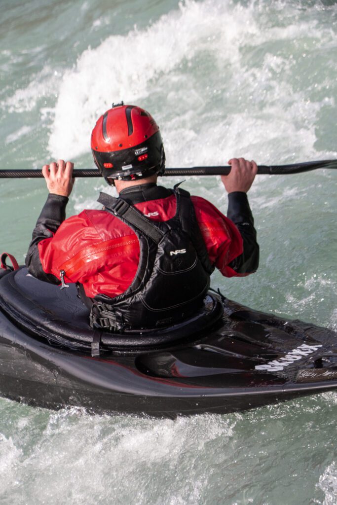 A kayaker in a black Waka skuxx shown from the back, eddying out, edging to the right side.