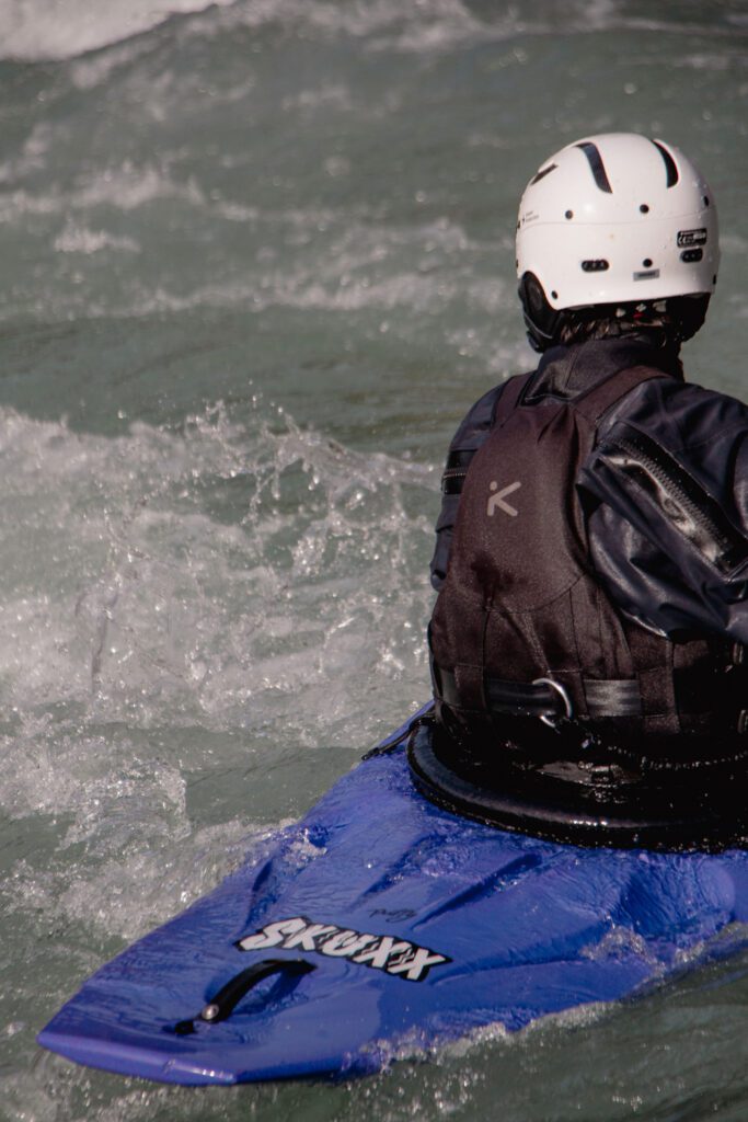 A kayaker in a purple Waka Puffy Skuxx, shown from the back, about to surf a wave.